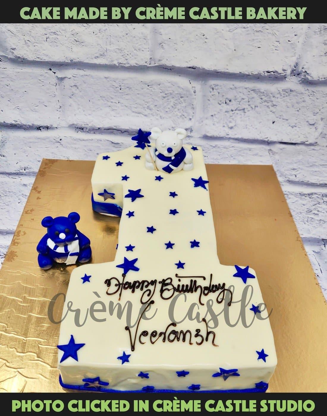 A cake for first birthday in the form of Number 1 in white theme with blue stars sprinkled all over the cake. 